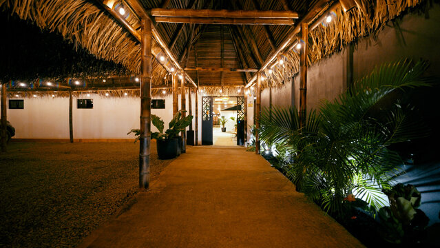Resort walkway illuminated at night, featuring a bamboo and thatch roof structure leading to an inviting entrance