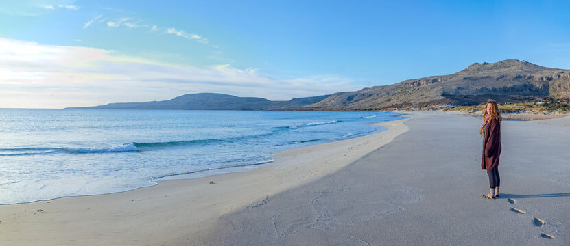 Simos Beach, Elafonisos, Greece: Woman standing on a sandy beach with mountains in background