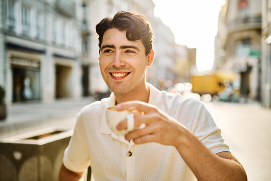 Portrait of a smiling young man guy with a coffee cup in a coffee shop or a restaurant in the city, tourists visiting destination, summer trip exploring, posing with a backpack