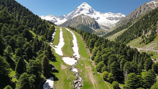 Green Mountain Slope With Snow Patches And Rocky Stream Below Snow Capped Peak