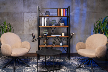 Podcast setup with two chairs, microphones, and a bookshelf in a simple room © MartaKlos