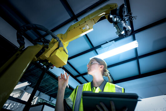A robotics engineer uses a tablet to program a robot with a machine vision system, while her colleague calibrates the end-of-arm tooling on another unit in a system integration lab.