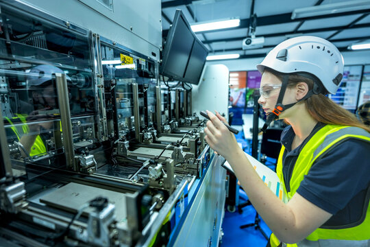 A robotics engineer uses a tablet to program a robot with a machine vision system, while her colleague calibrates the end-of-arm tooling on another unit in a system integration lab.