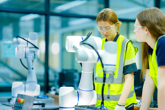 Two female engineering students in a high-tech university lab collaborate on a robotics project, learning hands-on programming skills for the future of industrial automation.