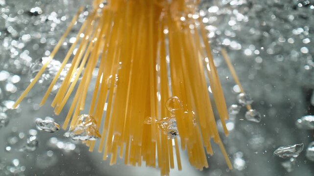 Raw Spaghetti Thrown into Boiling Water Breaks Through the Water's Surface, While Air Bubbles Rise Upward - a View from Inside the Pot