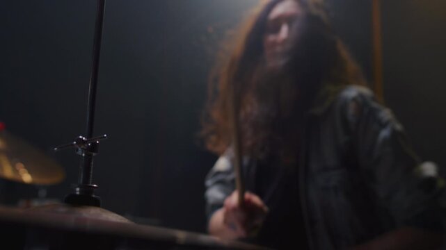 Portrait: female with long curly hair plays the drums. Girl is rehearsing in a studio with drumsticks. Face of a beautiful musician girl, showcasing skill and energy. Underground indie slow motion