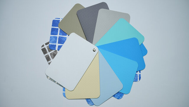 PVC pool liner sample swatches of textures and finishes, including classic blue mosaic tile patterns, modern solid aqua and sky-blue tones, light gray, beige, and neutral shades