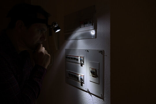 During a power outage a man with a headlamp examines his electrical panel.