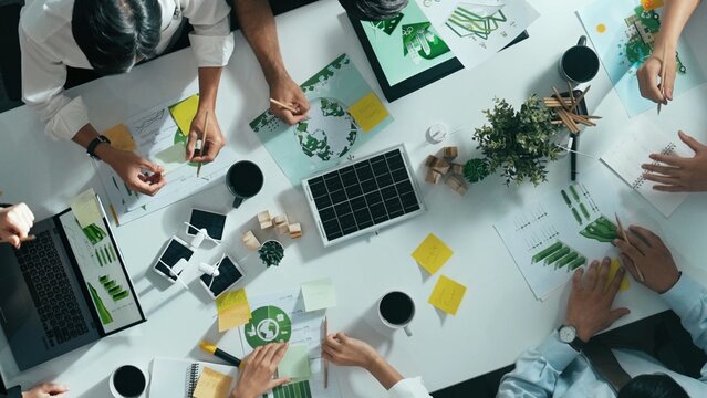 Top down view of business team discussing about using clean energy and sustainable investment at meeting table with wind mill, document with environmental graph and wooden house model. Alimentation.