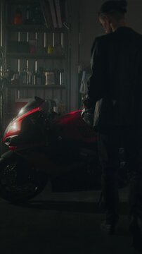 Rider in Leather Jacket Prepares For Ride. Once Seated, Man Assumes Aerodynamic Stance, Gloved Hands Ready Turn Ignition and Bring Powerful Machine Life. Man and Machine. Slow Motion. Vertical Shot.
