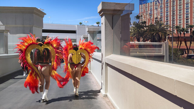Two performers dressed in flamboyant feather showgirl costumes and heart wings walking outdoors on a pedestrian bridge in Las Vegas Nevada on a sunny day