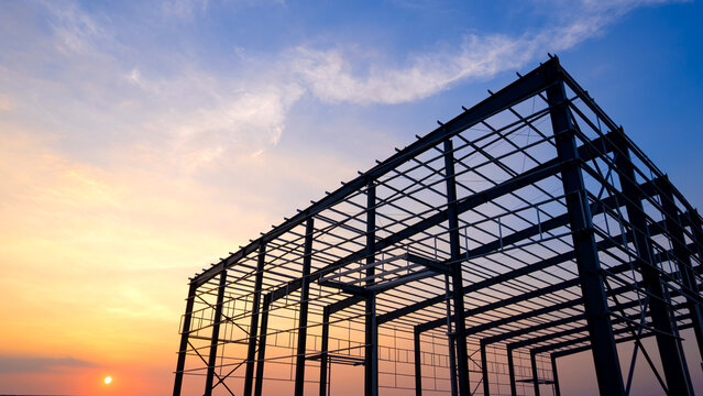 Silhouette steel structure of industry warehouse factory building with metal framework in construction site against sunset sky background, Low angle view with copy space