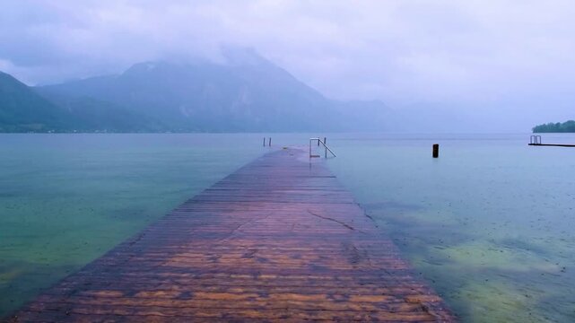 Moody and atmospheric rainy day at a tranquil mountain lake with a wet wooden dock.\
