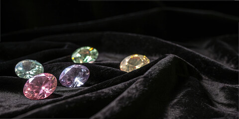 Colored stones are arranged on a black fabric surface. The stones reflect light and show various colors. The setting is bright and highlights their shine