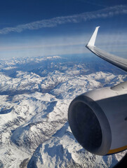 Photo of a beautiful landscape of the snow-capped Alps mountains in Italy from the window of a flying airplane with a view of the wing and turbine. © shchus