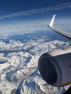 Photo of a beautiful landscape of the snow-capped Alps mountains in Italy from the window of a flying airplane with a view of the wing and turbine.