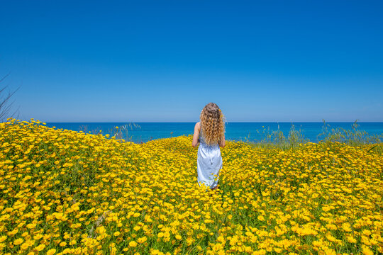 Blonde woman is standing in a beautiful flower field near beach.