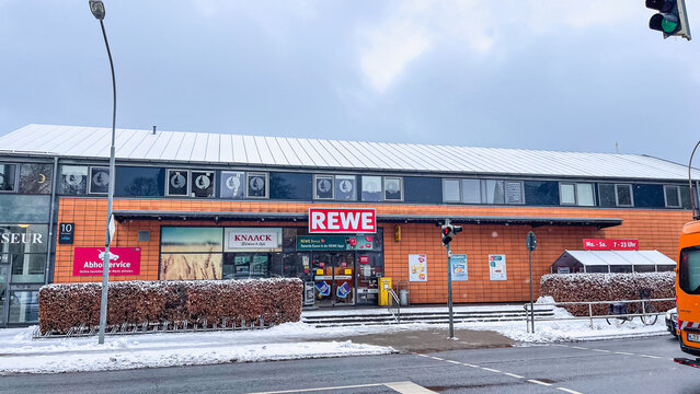 February 11, 2026, Lubeck, Germany: Rewe supermarket entrance on snowy street with hedges