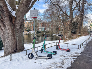 Naklejka premium February 18, 2026, Lubeck, Germany: Electric scooters parked in snow at riverside sharing station