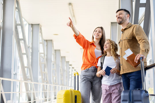 Smiling parents and daughter looking ahead at airport terminal, standing with suitcases and ready for family holiday trip and exciting vacation abroad
