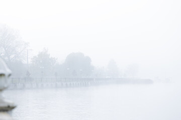 Fototapeta premium Misty morning over a calm lake with a distant pier and trees shrouded in fog