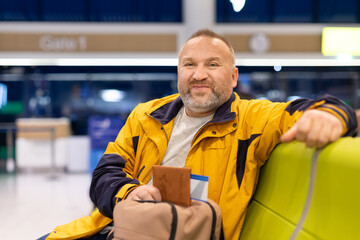 Relaxed adult caucasian man sitting in airport terminal with passport and bag. Confident traveler...