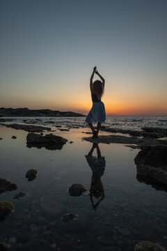 Silhouette of woman with reflection in water mirror at sunset.