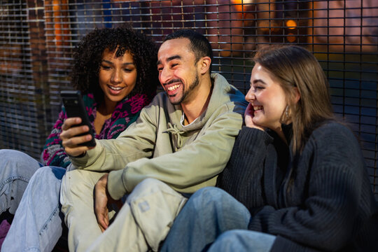 Diverse friends enjoying mobile phone content outdoors at night