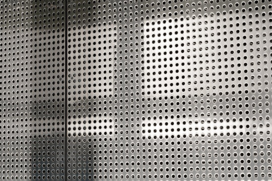 Panel consists of symmetrical perforated holes on silver metallic background emphasizing abstract and industrial geometry concepts