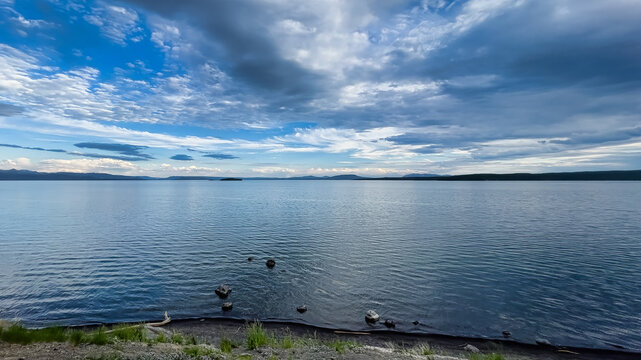 Calm evening view over Yellowstone Lake with soft ripples, distant mountains, and dramatic cloud layers across a wide blue horizon.