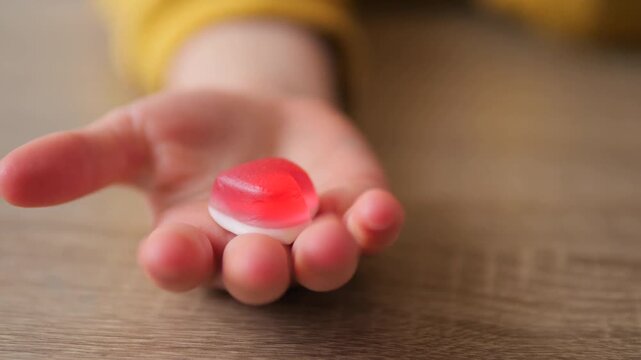 child holding a heart-shaped gummy candy in their palm Slow motion 180 fps. A close-up lifestyle sequence capturing a small red and white candy held by a toddler
