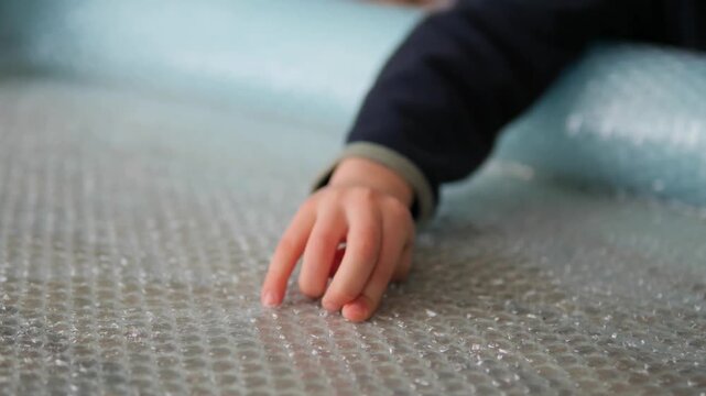 Close-up of child's hand exploring bubble wrap texture in 4K. Young boy's fingers feeling and pressing on plastic packing material, illustrating tactile sensory processing and mindful exploration