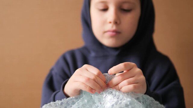 Child using bubble wrap for sensory stress relief 4K. A close-up, pensive shot of a young boy's hands popping plastic bubbles, illustrating tactile therapy, calming sensory play, and mental wellness