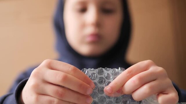 Slow motion child popping bubble wrap at 180 fps. Detailed high-frame-rate footage of a young boy's hands focused on tactile sensory play, stress relief, mental health support, and calm concentration