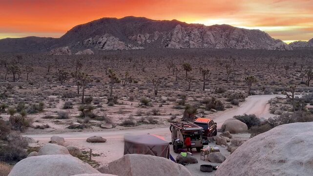 Morning brings a vibrant sky as campers set up a teardrop trailer for biking and exploring Joshua Tree National Park in California.