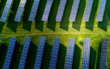 Fototapeta premium Aerial view of a vast solar farm with rows of photovoltaic panels on green grass