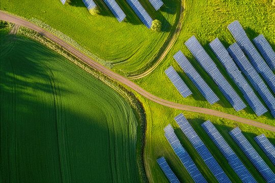 Aerial view of a vast solar panel farm nestled within lush green agricultural fields