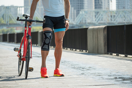 Close up of male cyclist leg with knee brace walking with bicycle