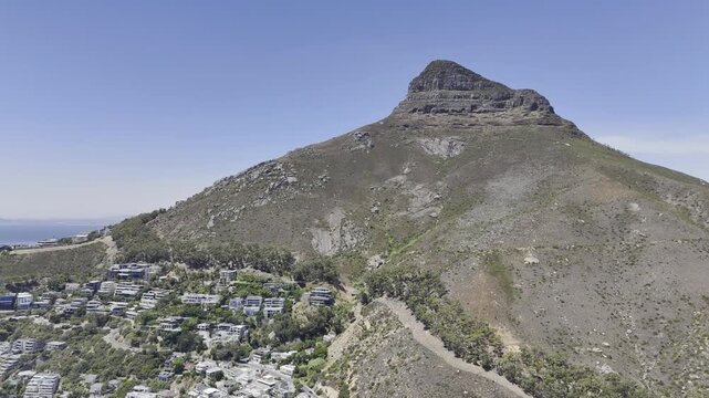 Drone flies north toward Lion's Head with luxury houses at the base on a sunny day in Cape Town, South Africa