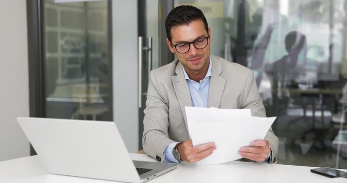 Positive handsome business executive man analyzing sales reports, company income. Male accountant in glasses reviewing paper analytics, using laptop computer, smiling