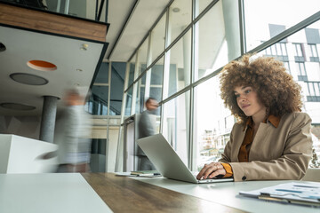 Businesswoman typing on laptop in busy modern office