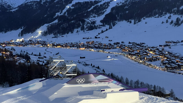 Livigno, Italy - February 20, 2026: Milano Cortina 2026 Olympic slopestyle course with illuminated jump and snowy village lights at dusk in Alps.