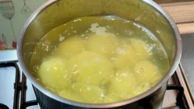 Boiling peeled potatoes in pot on gas stove, golden chunks simmering in bubbling water, gentle steam rising, home cook prepping.
