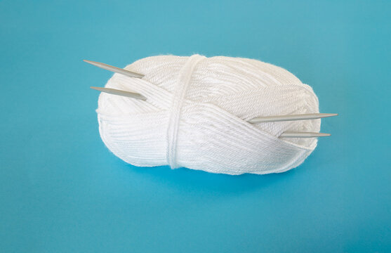 A new  skein of white yarn with a pair of knitting needles inserted into it.