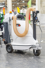Large white industrial floor cleaning machine with extendable hoses, located in a warehousemanufacturing facility The machine has mobility wheels, control panel, and is under even fluorescent light