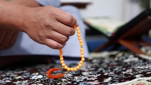 Close-up of hands doing dhikr using prayer beads with the Koran on the background as a background. Hands are praying. A man performs dhikr while holding prayer beads. A Muslim's worship activity