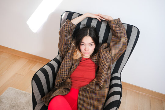 Woman relaxes in striped chair wearing oversized coat and red stocking