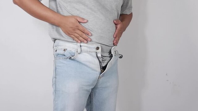 A man tries to button his pants, but his protruding belly prevents him from doing so. His protruding belly is getting bigger. Obesity, diet. Health Care