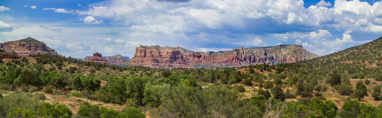 Fototapeta premium red rock formations near Sedona, Arizona under a clear blue sky. The landscape features greenery and distant mountains with clouds.