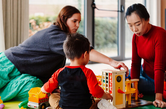 women and child playing with toys indoors on colorful floor mat